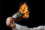 If This Man Thinks Inflation is Back, Worry Male hand close-up, holds burning money in hands, burning US dollars. Black background, isolate. The concept of inflation, a decrease in the purchase of foreign currency, and devolution.